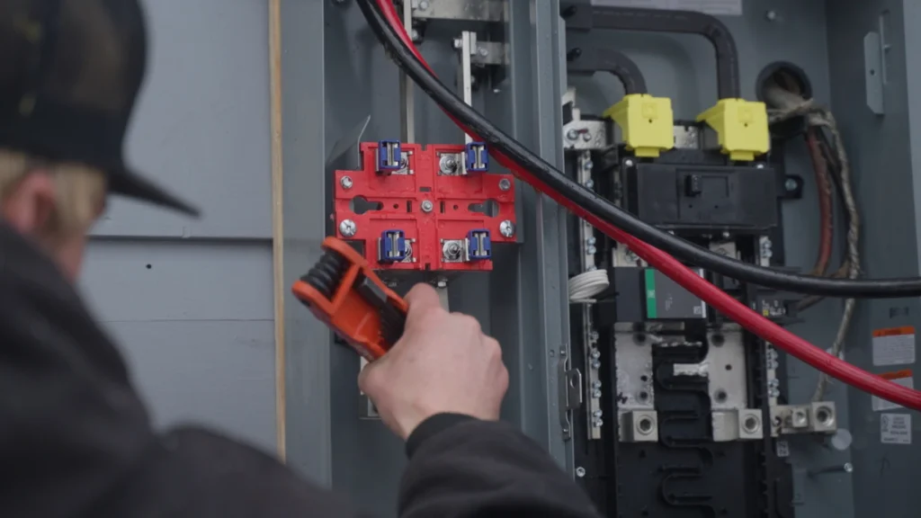 A person uses a wrench to adjust or repair electrical components inside an open electrical panel with various wires and circuit breakers visible.