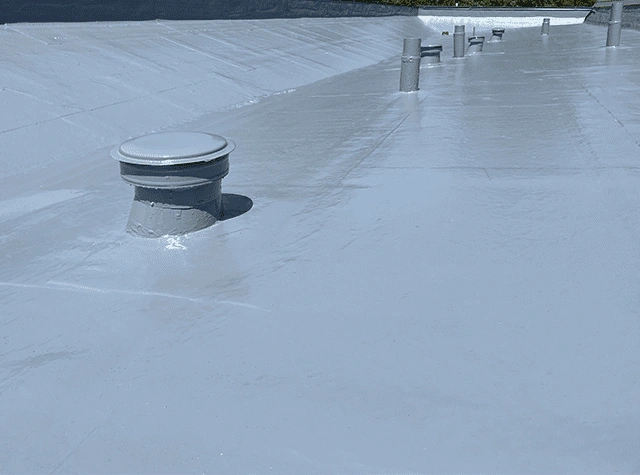 A flat rooftop with a smooth, reflective, light gray coating and several round vent pipes protruding from the surface. The coating appears clean and newly applied.