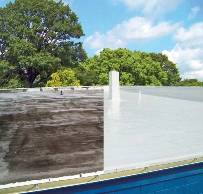 A flat rooftop is shown split down the middle, with one side old and dirty, and the other side clean and freshly coated in white, demonstrating a before-and-after roof restoration. Trees and blue sky are in the background.